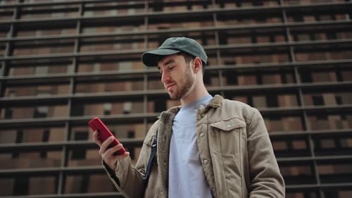 Young Man Using Mobile Phone in the City in Front of Modern Corporate Urban Office Building