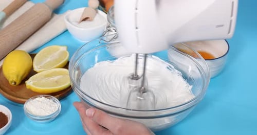 Woman whisking cream with hand mixer at light blue table, closeup. Camera zooming in