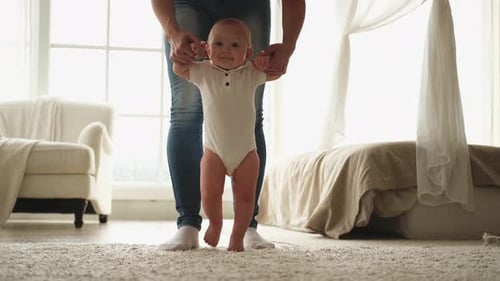 Mother Helping Baby Learn to Walk Indoors