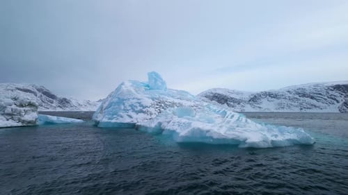 Massiver blauer Eisberg, der in ruhigen arktischen Gewässern unter bewölktem Himmel schwimmt