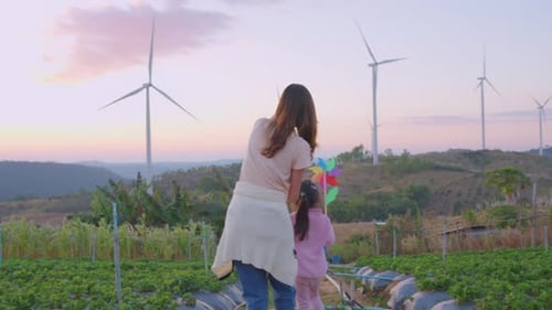 Asian mother walking with young kid daughter in the wind turbine field.