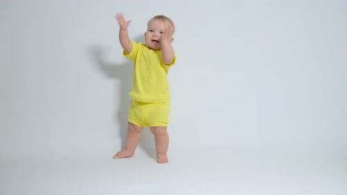 das Baby, das auf seinen Füßen steht, klatscht mit einem sehr zufriedenen Gesicht in die Hände