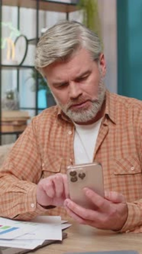 Man Reviews Charts at Desk with Phone Frustration