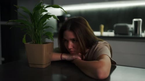 A Sad and Thoughtful Brunette Girl in a Beige Tshirt Sits Leaning on a Black Dining Table in the
