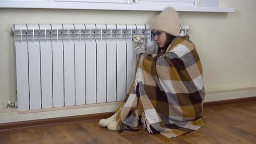 A Young Woman Sits at Home and Hugs a Radiator Because of the Cold
