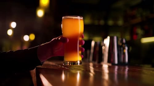 Closeup on a Wooden Bar Table Guy Holds a Glass of Light Beer Warm Lighting Light