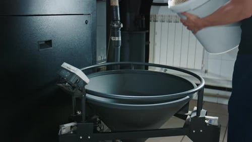 Arbeiter gießt grüne Kaffeebohnen in den Trichter der Röstmaschine