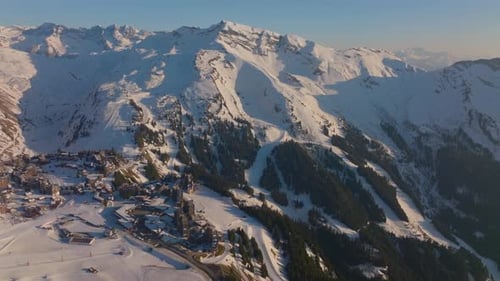Aerial Shot Of A Snowy Mountain Range With A Ski Resort And Alpine Trees Below