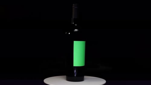 Wine or alcohol bottle with chroma green screen labels spinning on turntable stand in studio with bl