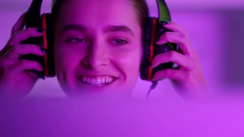 Smiling woman gamer with headphones looking at screen