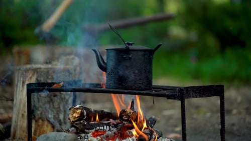A Camping Kettle Sits On A Grate Over A Fire In The Forest