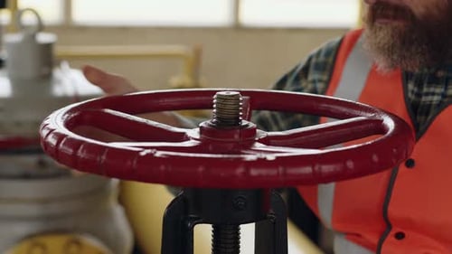 Worker Adjusting Red Industrial Valve with Hand Wearing Safety Vest in Workplace