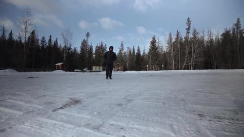 Mann mit Sonnenbrille und Winteroberbekleidung mit Rucksack geht auf einem schneebedeckten Parkplatz spazieren
