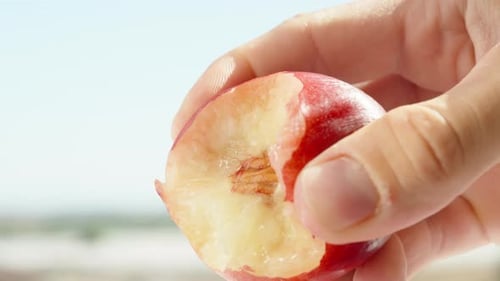 A man clutches a bitten nectarine in his hand in close-up, juice flows from it.