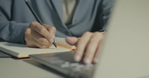 Adult Writing in Notebook Next to a Laptop