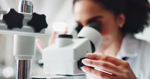 Woman Adjusting Focus of Microscope in Lab