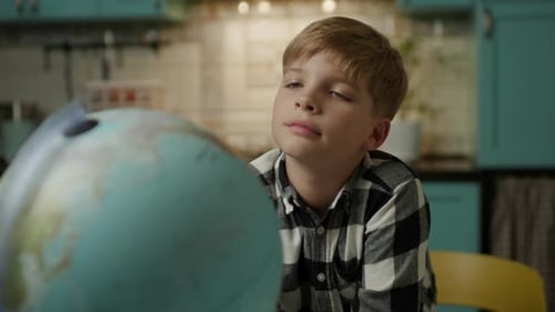 Pensive Boy Looks at Globe Inside a Home