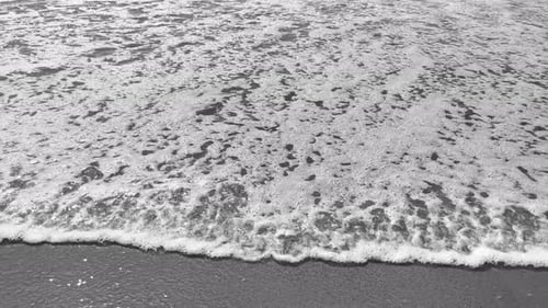 Grayscale Footage of Ocean Surf Gently Washing Onto the Sandy Shore The Foamy Wave Edges Create a