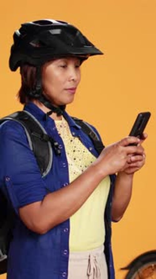 Woman with Helmet Looks at Smartphone by Bicycle