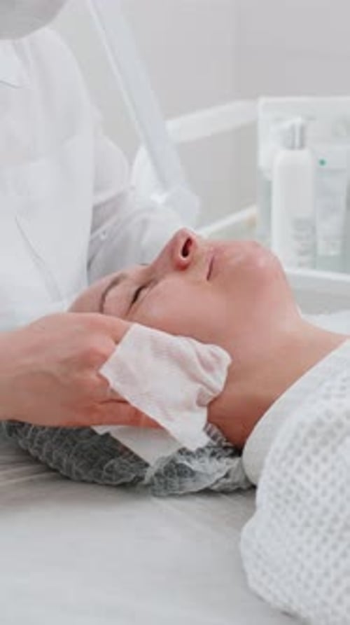 Cosmetologist Doctor Wipes Woman Face and Neck Cleaning Procedure with Cotton Pads in Beauty Clinic