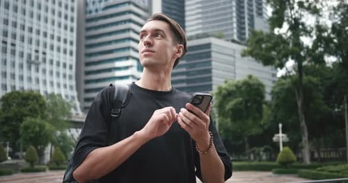 Male Tourist with Smartphone in Hand with Backpack Looks Around While Traveling in Big City Man