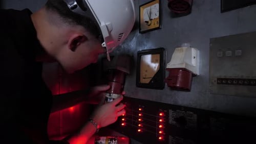 A Engineer or Electrician in a Helmet Works or Repairs Industrial Equipment