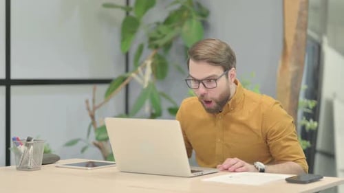 Young Man Celebrating Online Success on Laptop in Office