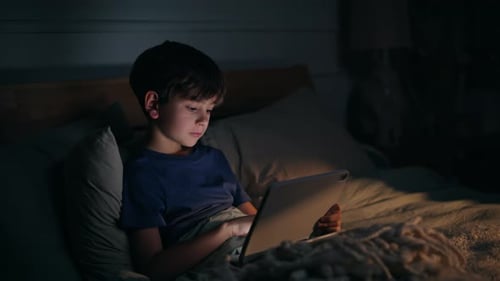 Tableta con desplazamiento Night Boy acostada en un acogedor dormitorio, primer plano, adicto al contacto de un niño
