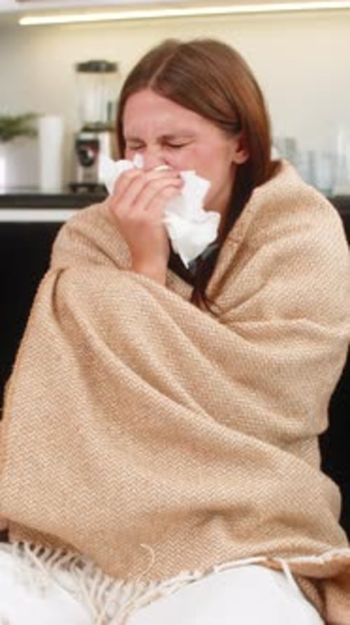 Woman With Blanket Blowing Nose While Sitting on Couch