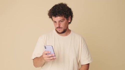 Surprised man with mobile phone in his hands in studio on beige background