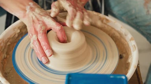 A female potter works on a potter's wheel, making a ceramic pot from clay in a pottery workshop.