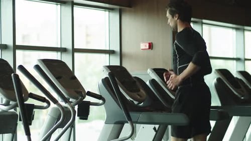 Closeup Serious Bodybuilding Man Running On Treadmill In Sport Club. Side View Sporty Male Athlet...