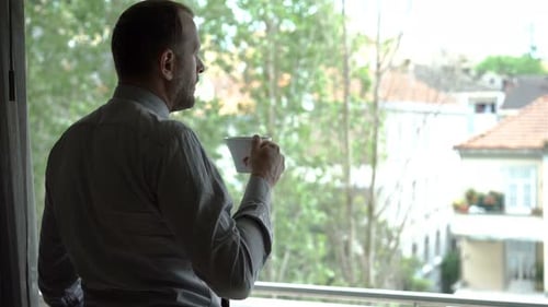 Young businessman enjoying coffee at home admiring city view from window