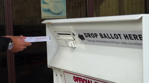 Young Man Drops Mail-in Ballot Letter in Slot at Official Voting Box with Drop Ballot Here Sign