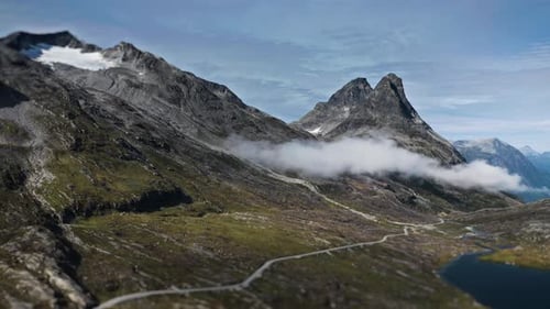 A narrow mountain road winds through the bleak Nordic landscape. Snow-capped mountains tower in the