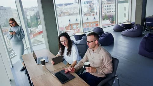Les collègues masculins et féminins sont assis au bureau avec des tasses à café mais continuent à travailler.