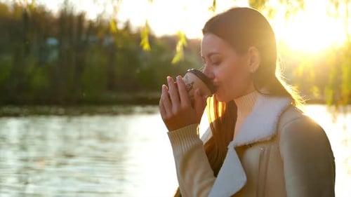 Woman Drinks Coffee Near Lake During Sunset