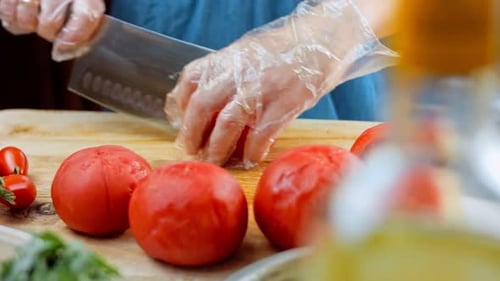 Chef in a Red Apron is Cutting Tomatoe in a Pot is on the Table Next to It