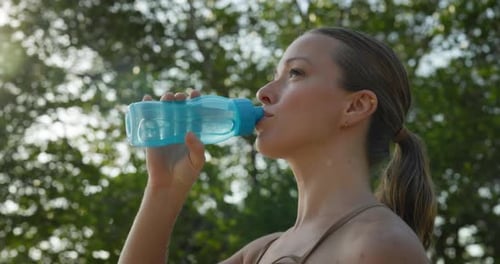Portrait of Attractive Lady in Sports Bra Sips Water From Bottle in Summer Park