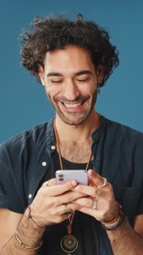 Smiling man using mobile phone, typing massages isolated on blue background in studio