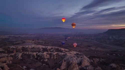 Drone view of dozens of balloons taking off at twilight, illuminated by burner flames in Rose Valley