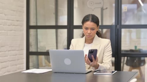 Young Woman Using Laptop and Phone at Desk