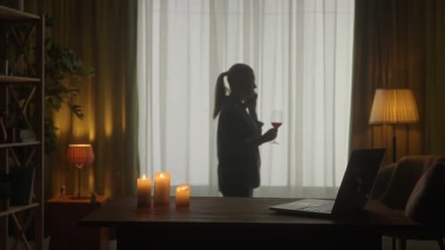 A Woman is Drinking Wine and Talking on the Phone Burning Candles and a Laptop are on the Table Dark