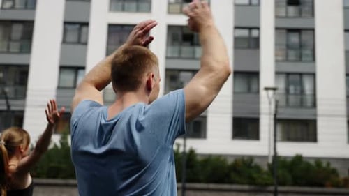 A Man and a Girl Play Sports Against the Background of the Windows of a Residential Complex
