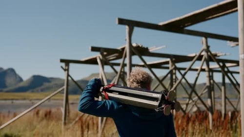 Man with Camera Tripod Walking Through Grassy Field