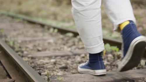 Eine Frau geht in Turnschuhen über die Schwellen der Bahnstrecke, Nahaufnahme, Kamera, Ein Spaziergang in der