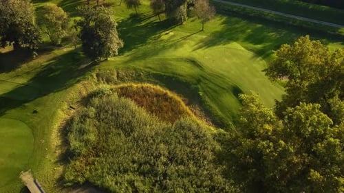 Aerial establishing drone shot flying upfront about trees showing golf course with pond during sunny