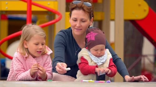 Mama im Park mit ihren Kindern unterhält sie, indem sie mit farbigen Kreiden zeichnet