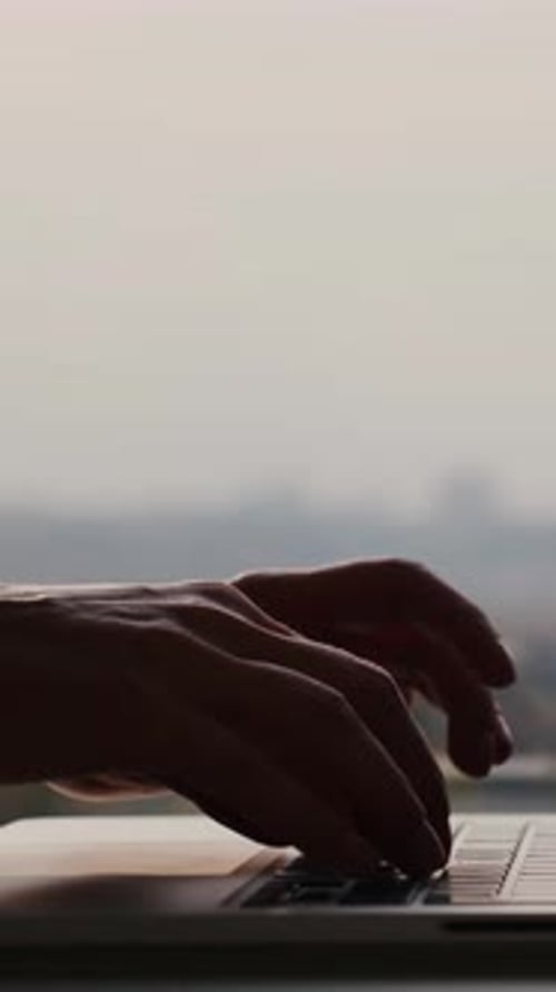 Close up fingers typing on laptop computer keyboard in office. Vertical video