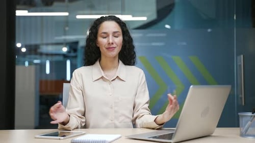 Businesswoman is meditating while sitting at a desk at a workplace in a modern business office.